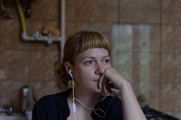 A young woman with earbuds in and resting her face on her hand.