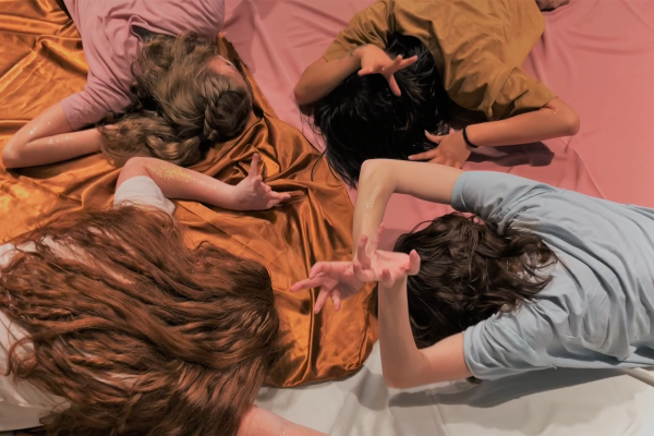 Four people laying facedown on colored fabric.