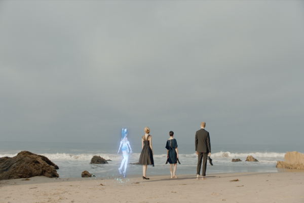 Four people (with one being a holographic image) walking on a beach