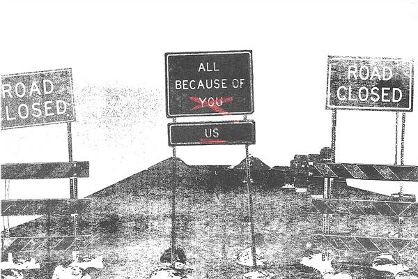 Road sign that says "All Because of You" with "You" crossed out and "Us" beneath it; signs on either side that say Road Closed