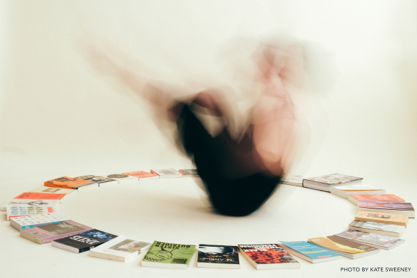 Person spinning/dancing in the center of a circle of books Photo by Kate Sweeney