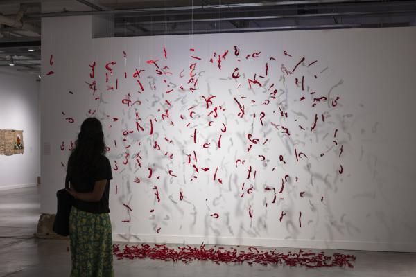 visitor looking at sculptural display of Illya's work--red letters in Persian/Farsi hanging from the ceiling in a deconstructed poem