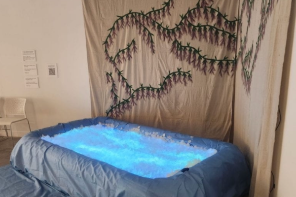 A glowing bue pool filled with fake flower petals and a painting of wisteria flowers behind it