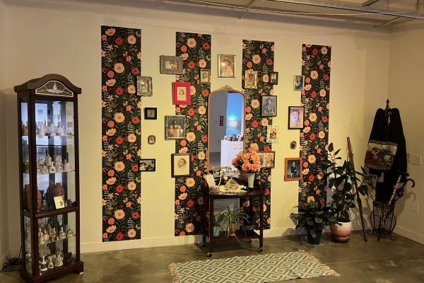 Wide shot of Crenshaw’s exhibition, featuring a family photo gallery wall, a wooden table spread, a wooden cabinet, and a coat rack.
