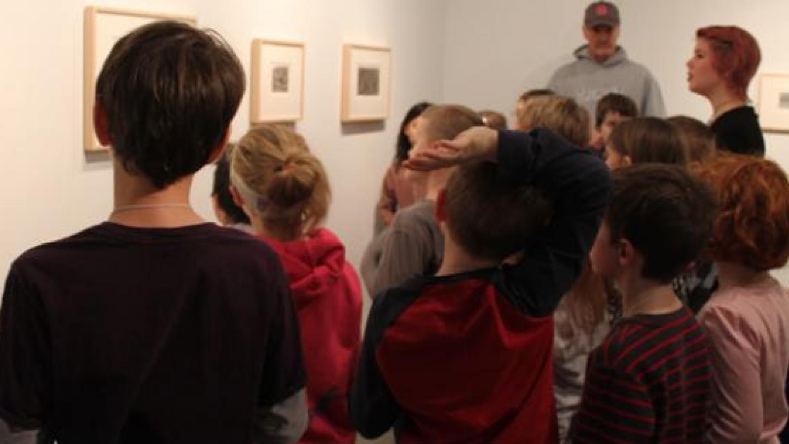 A group of people observe paintings on a gallery wall.