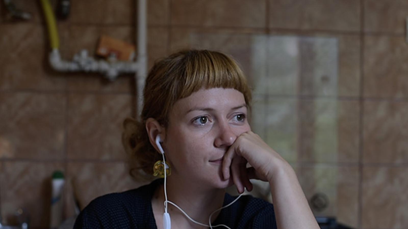 A young woman with earbuds in and resting her face on her hand.