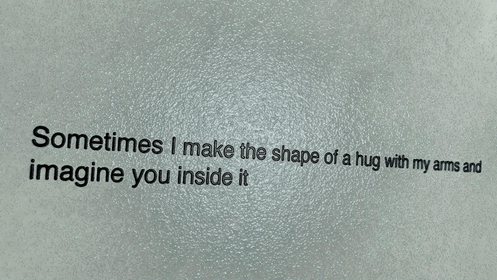 Black text on a bumpy grey background reads "Sometimes I make the shape of a hug with my arms and imagine you inside it"