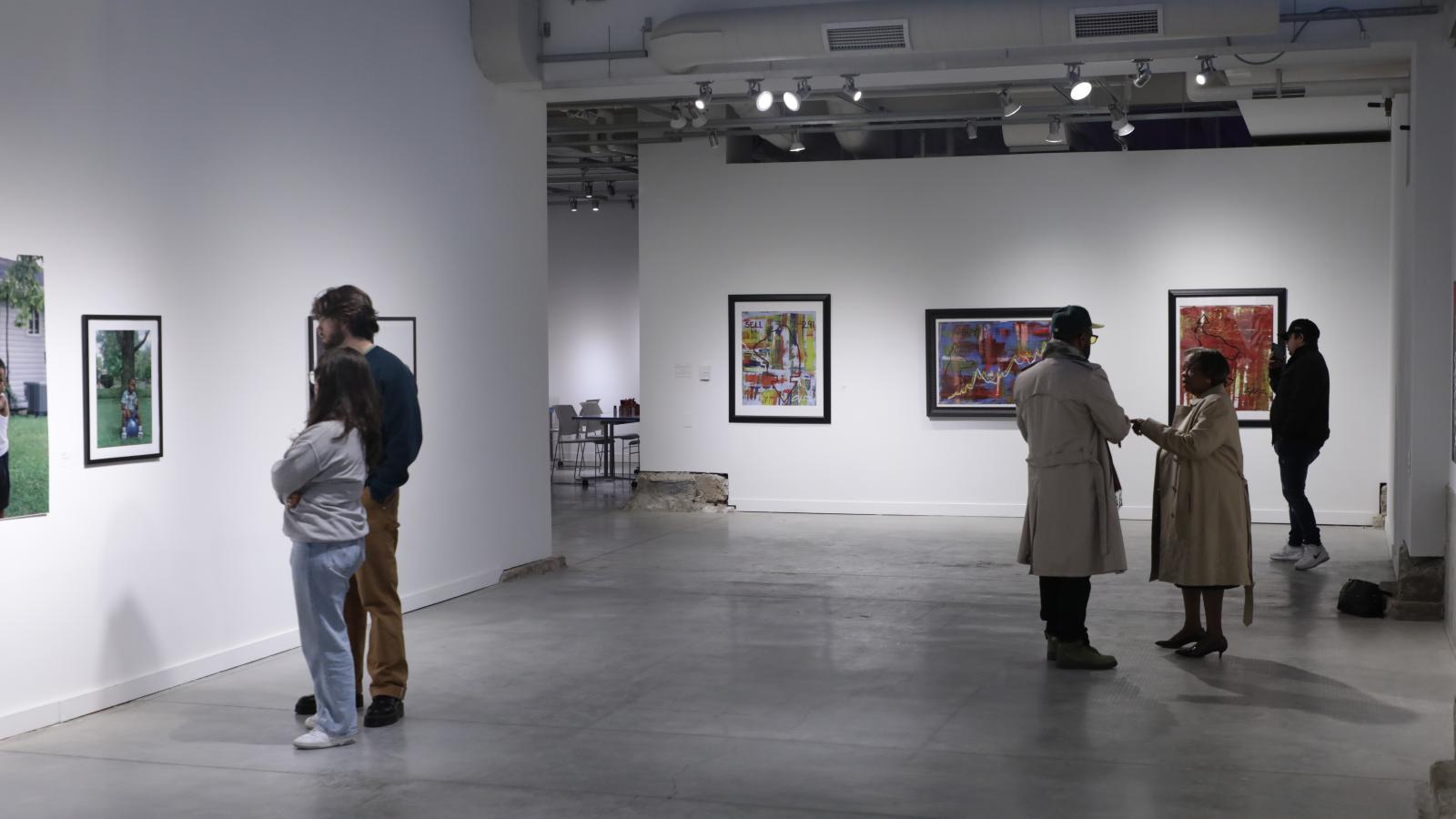 A photo taken in the gallery, three people are admiring artwork and two other people are in conversation.