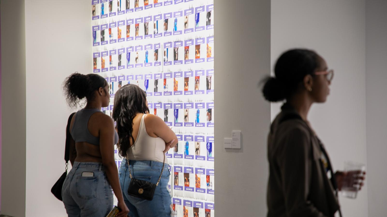 Visitors at the exhibition looking at wall of missing posters