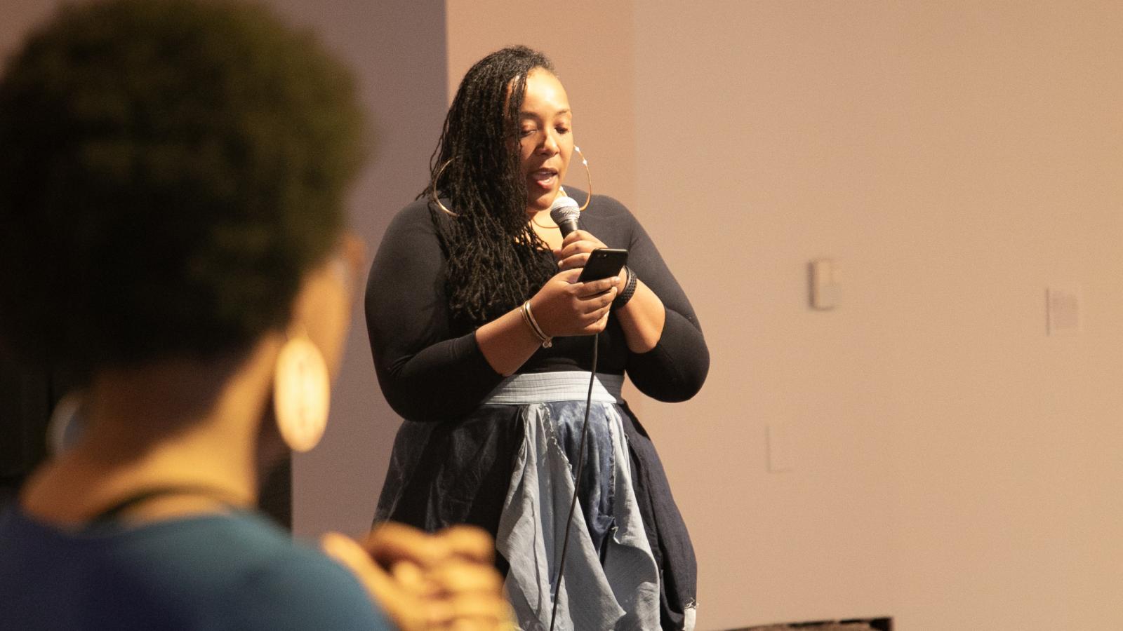 Tyiesha Radford Shorts stands holding a microphone, speaking into it 