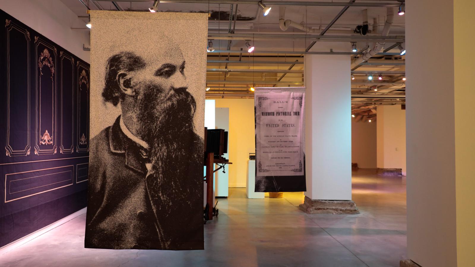 Two large banners hang from the ceiling, one a photo of James Presley Ball and the other a pamphlet cover 