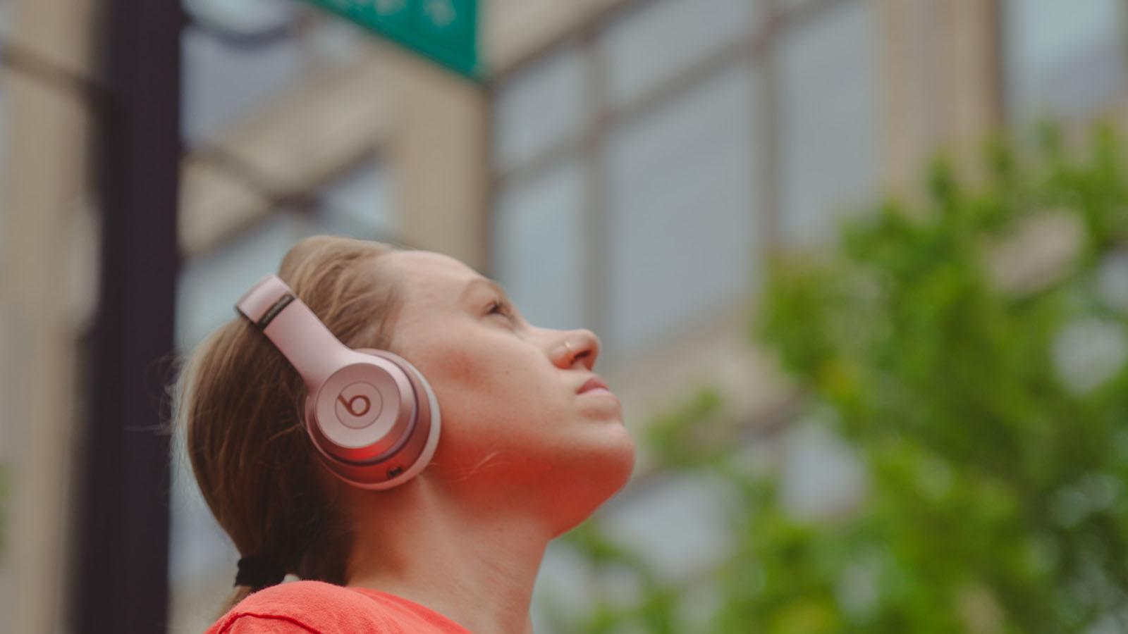 Woman outside with headphones on, looking towards the sky
