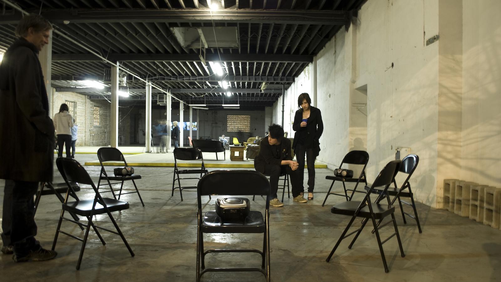 Brian Keith Sharrock, Untitled (come listen to yourselves), CD players, sound, metal chairs, video projection, 2009 – 2010