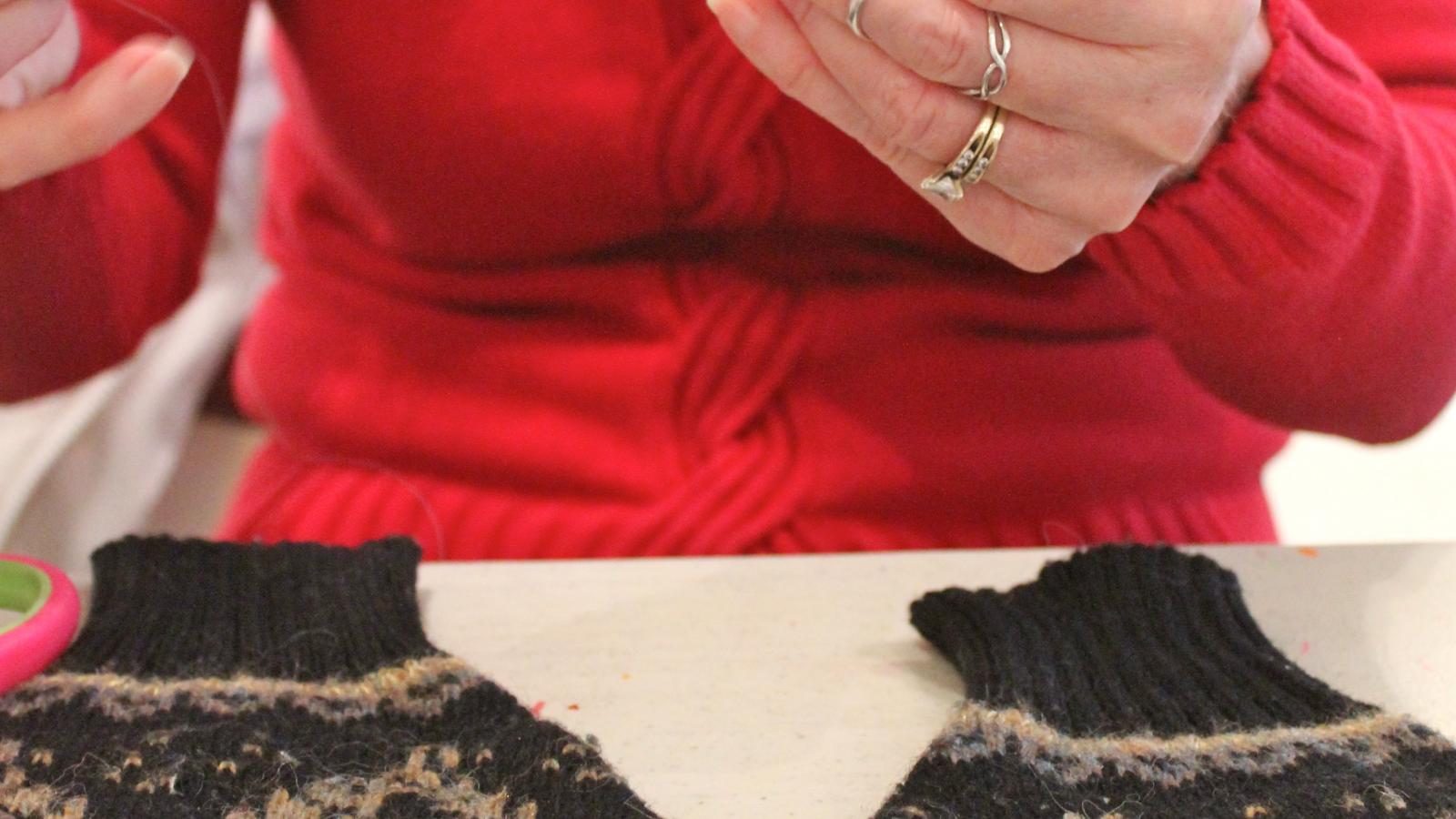 A person holds a piece of string in their hands. On the table beneath them is a pair of mittens
