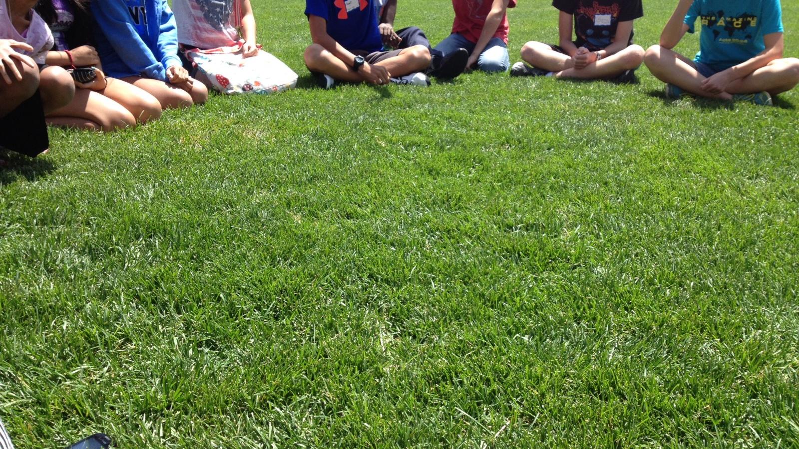 Young people sit on the grass at Summer Arts Camp 2014
