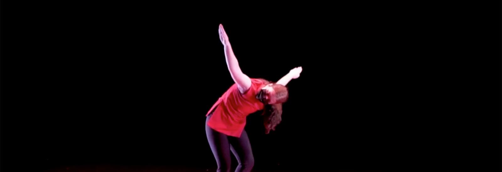 A dancer poses on a red floor in front of a black background.
