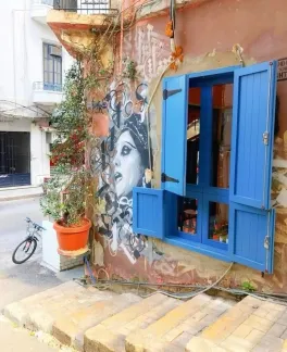 A blue door on an open window with a painting of Fairuz painted on the side